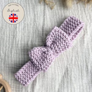 May include: A knitted lavender headband with a bow detail. The headband is made of a soft, textured yarn and is designed for babies. The image also includes a circular graphic with the text "PDF Pattern English" and a Union Jack flag.
