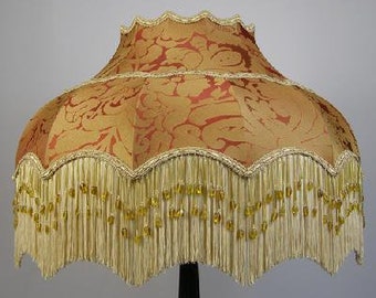 May include: A gold and red lampshade with a scalloped edge and fringe trim. The fringe is made of a light-colored material and has small beads woven into it.