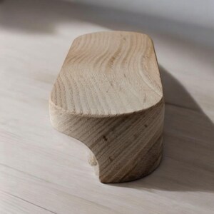 May include: A light wood, irregularly shaped, wooden pedestal with a smooth, slightly rounded top.