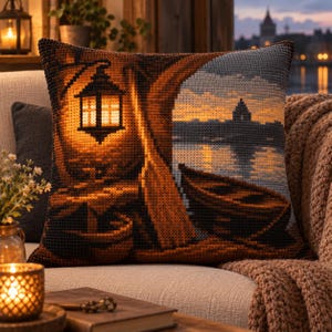 May include: A square throw pillow featuring a cross-stitch style design of a harbour scene at dusk. The image depicts a glowing lantern hanging near a wooden structure, a small boat resting on the shore, and a distant building silhouette over water.
