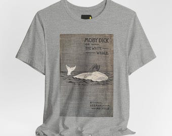 May include: A heather gray short-sleeve t-shirt featuring a rectangular graphic print of a white whale in water. The text reads Moby Dick or The White Whale by Herman Melville. The design has a textured, canvas-like appearance on the fabric.