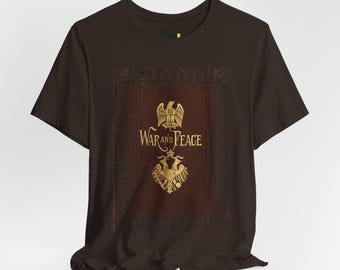 May include: A dark brown short-sleeve t-shirt featuring a central graphic of a book cover design. The print displays the text War and Peace in gold lettering, flanked by two golden eagle emblems, all set within a decorative dark red border.