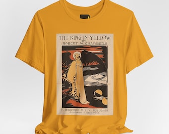 May include: A mustard yellow short-sleeve t-shirt featuring a rectangular graphic print of the book cover for The King in Yellow by Robert W. Chambers. The print depicts a cloaked figure with wings against a dark landscape and includes text.