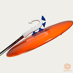 Op de afbeelding: Een oranje surfboard met een wit en blauw haakvormig opzetstuk. De haak heeft een gekartelde rand en is verbonden met een zilveren paal. Het surfboard is schuin geplaatst en toont zijn glanzende oppervlak.