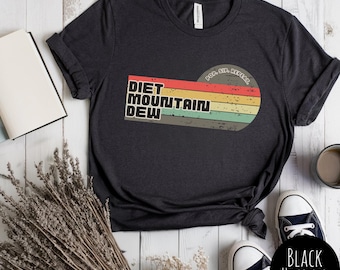 Puede incluir: Camiseta negra jaspeada con el texto "DIET MOUNTAIN DEW" en un diseño retro con un fondo a rayas. El diseño también incluye las palabras "POP. SIP. REPEAT.". La camiseta se combina con zapatillas de lona en blanco y negro.