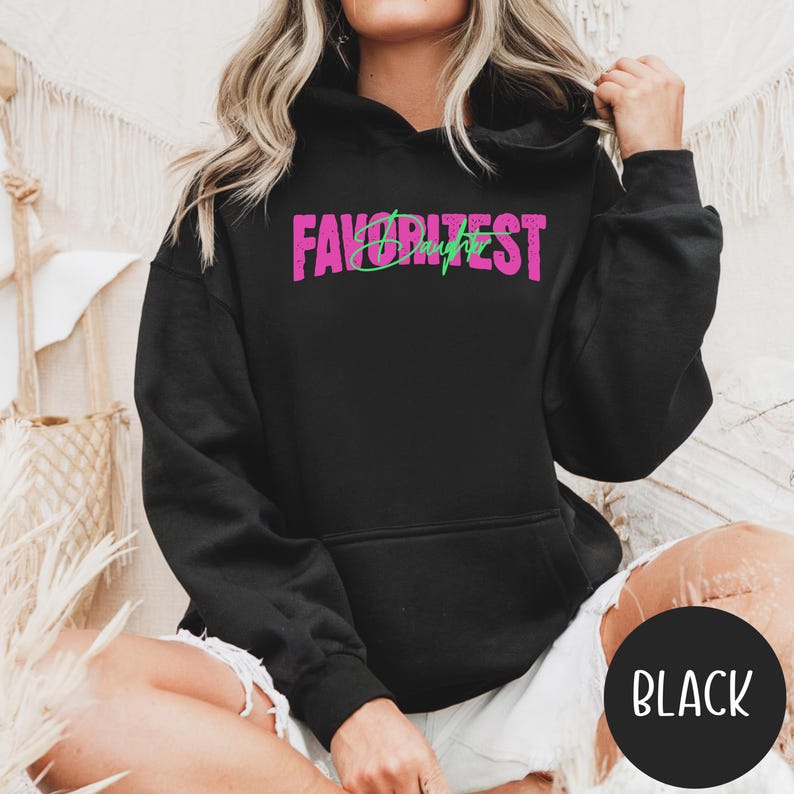 May include: Black hooded sweatshirt with the text "FAVORITEST Daughter" in pink and green. The sweatshirt has a drawstring hood and a kangaroo pocket. The word "BLACK" is in a black circle.