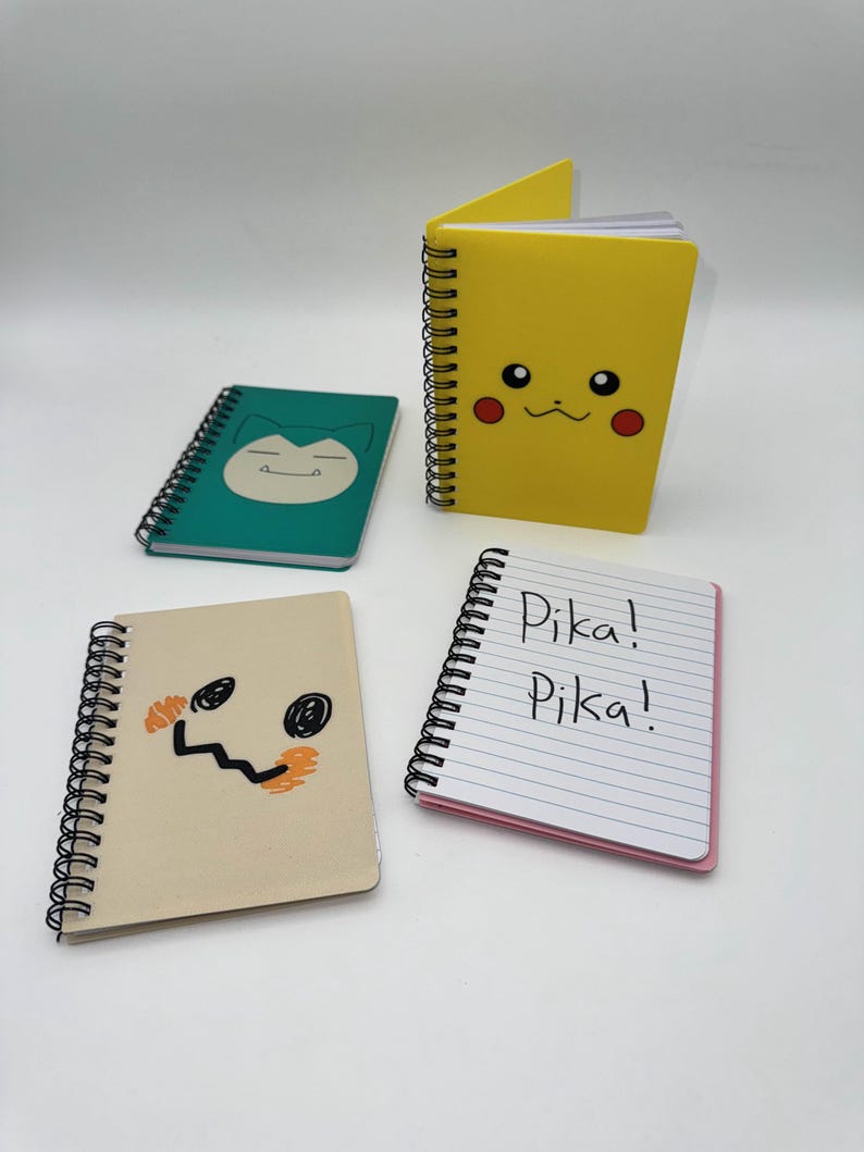 May include: Four spiral-bound notebooks with character designs. A yellow notebook features a Pikachu face, a green notebook has a Snorlax face, and a tan notebook has a Mimikyu face. A fourth notebook has the text "Pika! Pika!" on the lined pages.