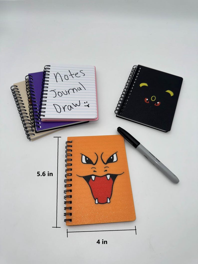 May include: A collection of spiral-bound notebooks. One orange notebook features a cartoon face, measuring 4 inches wide and 5.6 inches tall. Other notebooks are black, purple, and tan. One notebook has the words "Notes Journal Draw" written on the cover.