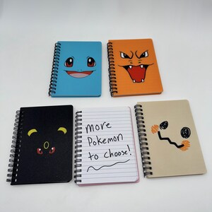 May include: Five spiral-bound notebooks with colorful covers featuring Pok&eacute;mon character designs. The notebooks include a blue Squirtle, orange Charizard, black Umbreon, tan Mimikyu, and a notebook with the text "More Pokemon to choose!"