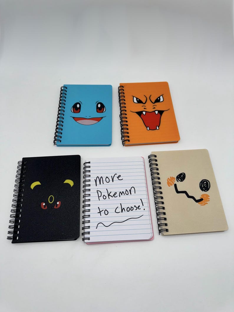 May include: Five spiral-bound notebooks with colorful covers featuring Pok&eacute;mon character designs. The notebooks include a blue Squirtle, orange Charizard, black Umbreon, tan Mimikyu, and a notebook with the text "More Pokemon to choose!"