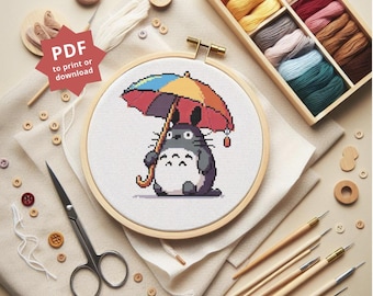 Puede incluir: Un patrón de punto de cruz con un Totoro de dibujos animados sosteniendo un paraguas colorido. El patrón se muestra en un aro de bordado de madera. La imagen también incluye hilo de bordar, agujas y otros materiales de artesanía.