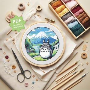 Könnte beinhalten: Ein Kreuzstichmuster mit Totoro aus dem Film Mein Nachbar Totoro, der vor dem Fuji steht. Das Muster befindet sich in einem runden Holzstickrahmen mit einer PDF-Download-Option.