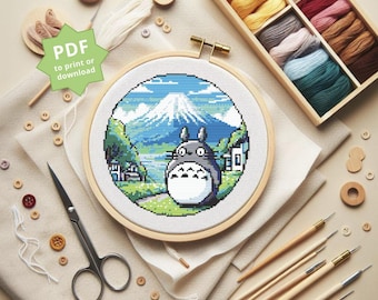 Puede incluir: Un patrón de punto de cruz con Totoro de la película Mi vecino Totoro, de pie frente al monte Fuji. El patrón está en un aro de bordado de madera redondo, con una opción de descarga PDF.