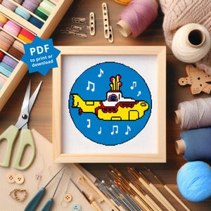 May include: A framed cross-stitch featuring a yellow submarine design on a blue background, surrounded by musical notes. The frame is made of light-colored wood. The text "PDF to print or download" is in a blue starburst.