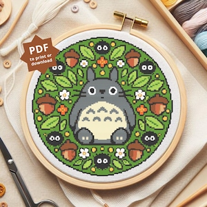 Peut inclure: Un cercle de broderie au point de croix avec un personnage de dessin animé gris, un ventre blanc, des feuilles vertes, des glands et de petites créatures noires. Le motif est sur un fond vert. Le texte "PDF to print or download" est visible.