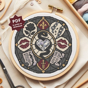 May include: A circular cross-stitch pattern in a wooden embroidery hoop featuring a central heart and snake motif surrounded by icons including a rose, lips, chains, a sword, and a fleur-de-lis. A dark red star-shaped tag reads PDF to print or download.