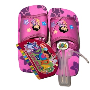 May include: Pink Dora the Explorer sandals with a star pattern and character graphics. The sandals have a strap and a tag with the show's logo. The sandals are new with tags.