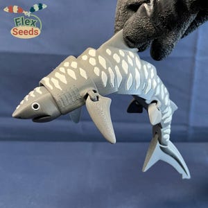 May include: A gray and white articulated shark toy with a segmented body and movable fins. The shark has a spotted pattern and is posed in a jumping position.