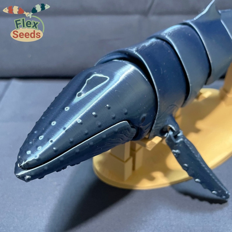 Puede incluir: Un modelo de ballena azul con una superficie texturizada y una cabeza detallada. El modelo est&aacute; sobre una base de madera.