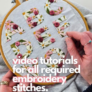 K&ouml;nnte beinhalten: Ein Stickrahmen mit den Buchstaben A bis F, bestickt mit wei&szlig;en, rosa und gr&uuml;nen Blumenmustern. Der Text "video tutorials for all required embroidery stitches" ist in Rosa und Wei&szlig; dargestellt.