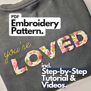 Könnte beinhalten: Dunkelgraues Sweatshirt mit gesticktem Schriftzug "you're LOVED". Das Wort "LOVED" ist mit weißen und gelben Gänseblümchen und rosa Blüten bestickt. Das Bild enthält auch den Text "PDF Embroidery Pattern" und "incl. Step-by-Step Tutorial & Videos."