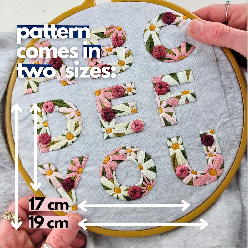 K&ouml;nnte beinhalten: Gestickte Buchstaben A bis V, jeweils mit G&auml;nsebl&uuml;mchen- und Rosenmotiven verziert, werden in einem h&ouml;lzernen Stickrahmen gezeigt. Der Text "pattern comes in two sizes" ist sichtbar. Die Stickerei misst 17 cm und 19 cm.