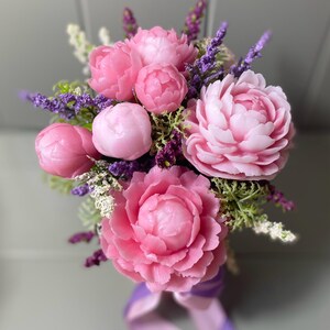 May include: A bouquet of pink soap flowers with lavender accents. The bouquet is tied with a purple ribbon and the text "Soap Bouquets UK" is visible at the bottom of the image.