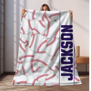 May include: White fleece blanket with a baseball pattern and the name "JACKSON" printed vertically in dark blue on the right side.