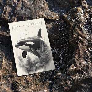 May include: A black and white drawing of an orca swimming in the ocean. The drawing is on a white card with the words "Waves of Grief" written in black at the top.