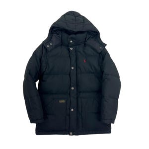 May include: A black puffer jacket with a hood, featuring a front zipper closure covered by a snap-button placket. The jacket has a small red embroidered logo on the left chest and a rectangular patch on the lower right pocket area.