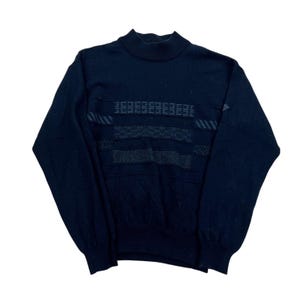 May include: A dark navy blue turtleneck jumper with geometric patterns across the chest. The jumper features a ribbed collar and cuffs, and a textured design. The overall style is vintage.