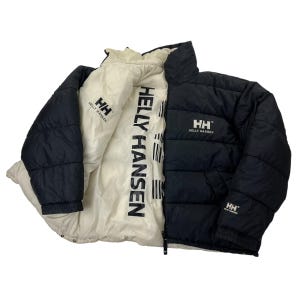 May include: A reversible puffer jacket featuring a black side with the white Helly Hansen logo on the chest and sleeve, and a cream-colored side with the black Helly Hansen brand name printed vertically along the front opening and a small logo.