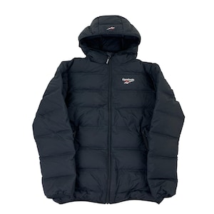 Op de afbeelding: Zwarte pufferjack met capuchon. De jas heeft een lange ritssluiting en het Reebok-logo in wit en rood op de borst. Ontworpen voor koud weer, heeft het een gewatteerd patroon.