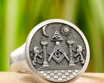 May include: A silver ring featuring a Masonic symbol design. The ring depicts a square and compass, an all-seeing eye, and two lions.