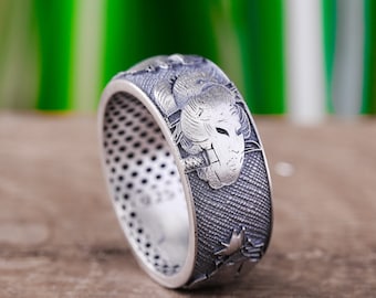 Könnte beinhalten: Ein silberner Ring mit einem komplizierten Design, das einen stilisierten Tierkopf zeigt. Der Ring hat eine strukturierte Oberfläche und ein detailliertes Muster.