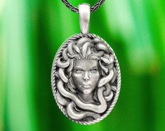 May include: A silver pendant necklace featuring a detailed depiction of Medusa, the Greek mythological figure with snakes for hair. The pendant is oval-shaped and has a rope chain.
