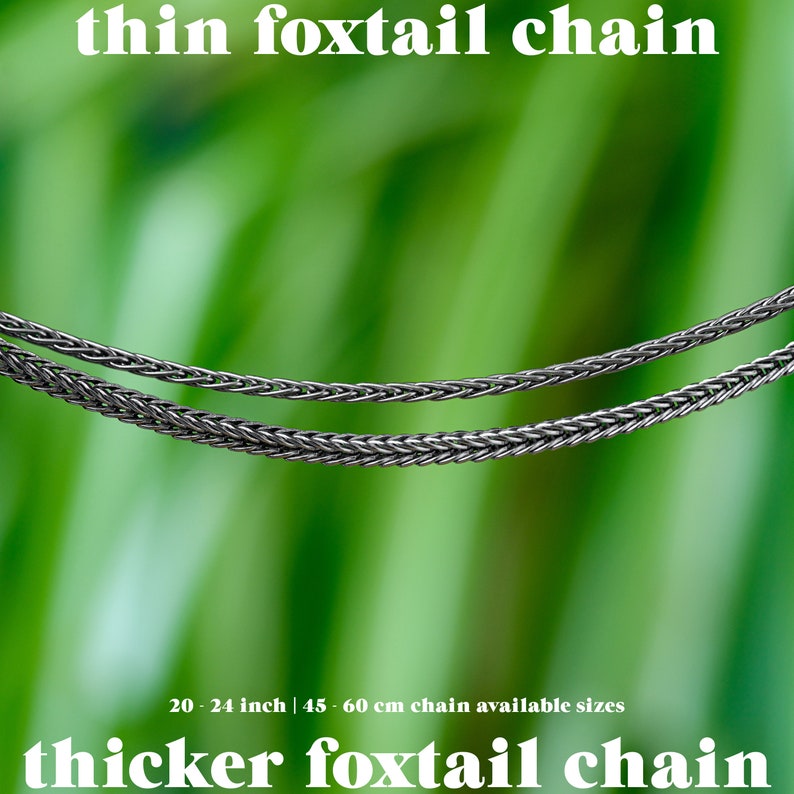 May include: Two silver foxtail chains are displayed against a blurred green background. The text "thin foxtail chain" and "thicker foxtail chain" are at the top and bottom. Available sizes are 20-24 inches.