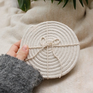 May include: A set of round, white, woven coasters tied together with twine. The coasters are made from natural materials and have a rustic, farmhouse aesthetic.