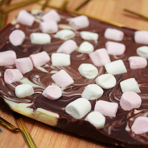 Puede incluir: Primer plano de una barra de chocolate con remolinos de chocolate blanco y negro cubiertos con malvaviscos rosas y blancos.