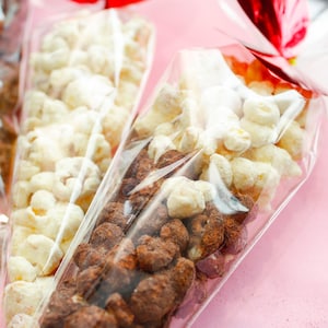 Può includere: Tre coni di plastica trasparente riempiti con diversi snack. Il cono a sinistra è pieno di noci ricoperte di cioccolato fondente. Il cono al centro è pieno di popcorn bianco. Il cono a destra è pieno di una miscela di noci ricoperte di cioccolato fondente e popcorn bianco.