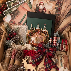 May include: A festive-themed craft supply box containing decorative paper sheets with Santa and candle illustrations, a dark green notebook, a pop-up gate card, lace trim, twine spools, nutcracker figurines, a plaid bow, and wooden reindeer.