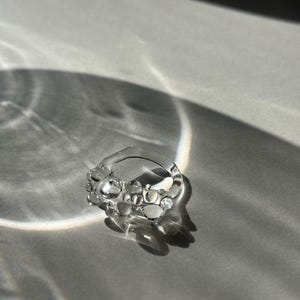 Könnte beinhalten: Ein silberner Ring mit einem einzigartigen Design, das mehrere kleine, runde, klare Steine ​​aufweist.