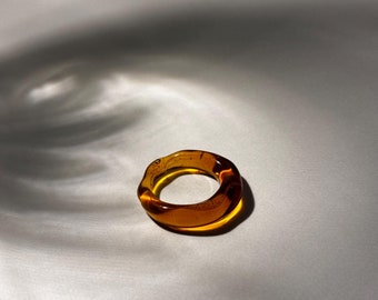 May include: A thick amber glass ring with a wavy, irregular shape.