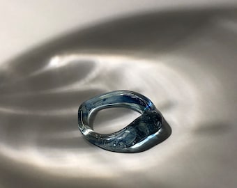 May include: A blue glass ring with a unique, organic shape. The ring is translucent and has a slightly cloudy appearance.