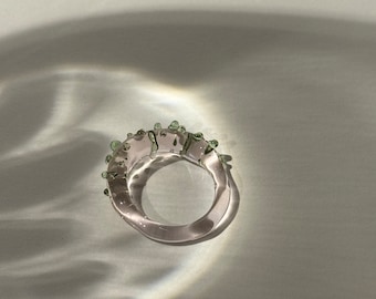 Op de afbeelding: Een transparante glazen ring met groene accenten. De ring is dik en heeft een afgeronde vorm.