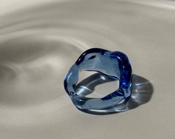 May include: A blue glass ring with an irregular, organic shape. The ring is translucent and has a slight shimmer.