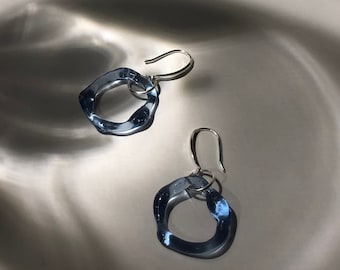 May include: A pair of blue glass earrings with silver hooks. The earrings are shaped like irregular circles.
