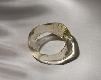 Op de afbeelding: Een transparante, golvende ring met een organische vorm. De ring is gemaakt van hars en heeft een subtiele glans.
