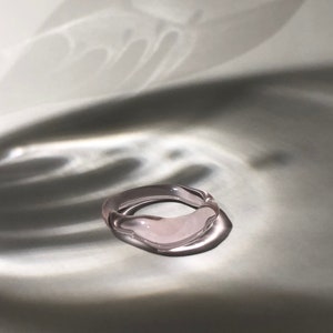 May include: A light pink glass ring with an irregular, organic shape.