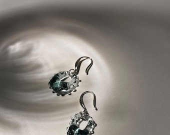 May include: A pair of silver hoop earrings with a clear glass design featuring a green swirl. The glass is textured and has a bubbly appearance.